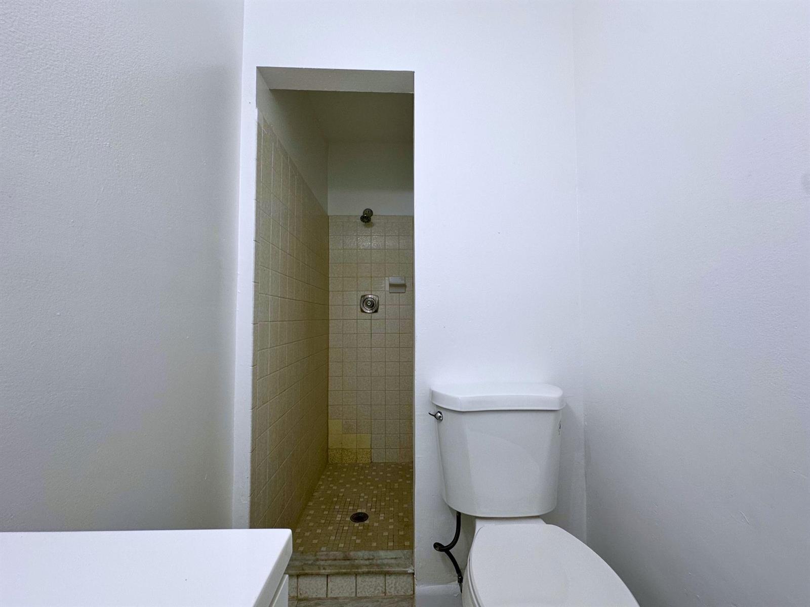 A bathroom features a white toilet next to a tiled walk-in shower stall — 329 Melody Lane, Lantana FL 33462, LANTANA, FL