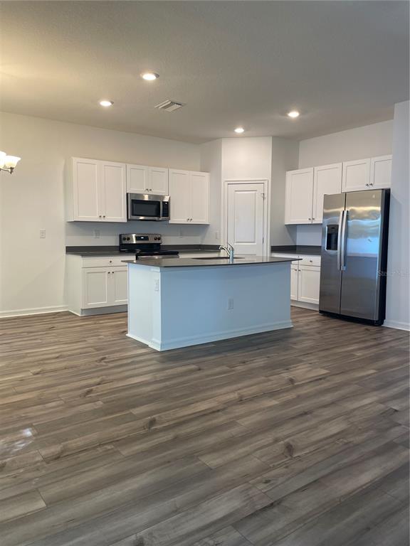 A kitchen features white cabinetry, stainless steel appliances, a center island, and wood-look flooring — 34772 MULRION DRIVE, ZEPHYRHILLS, FL