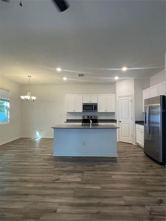 A kitchen features white cabinets, a central island, stainless steel appliances, and wood-look flooring — 34772 MULRION DRIVE, ZEPHYRHILLS, FL