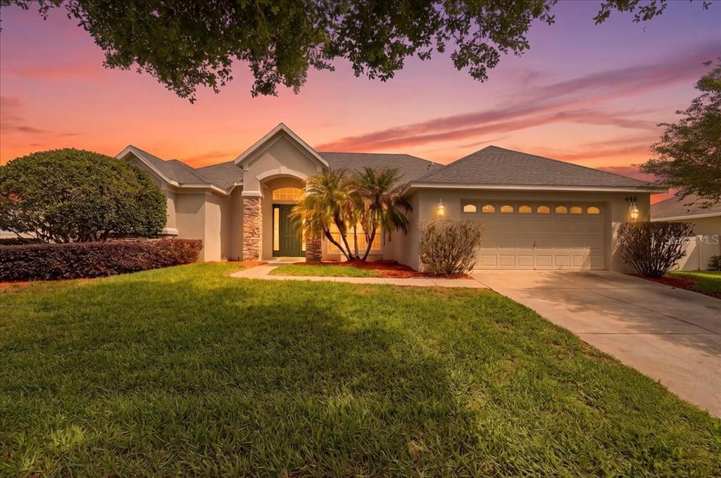 A single-story house with a beige stucco exterior, a two-car garage, and a landscaped lawn — 445 AMETHYST AVENUE, AUBURNDALE, FL