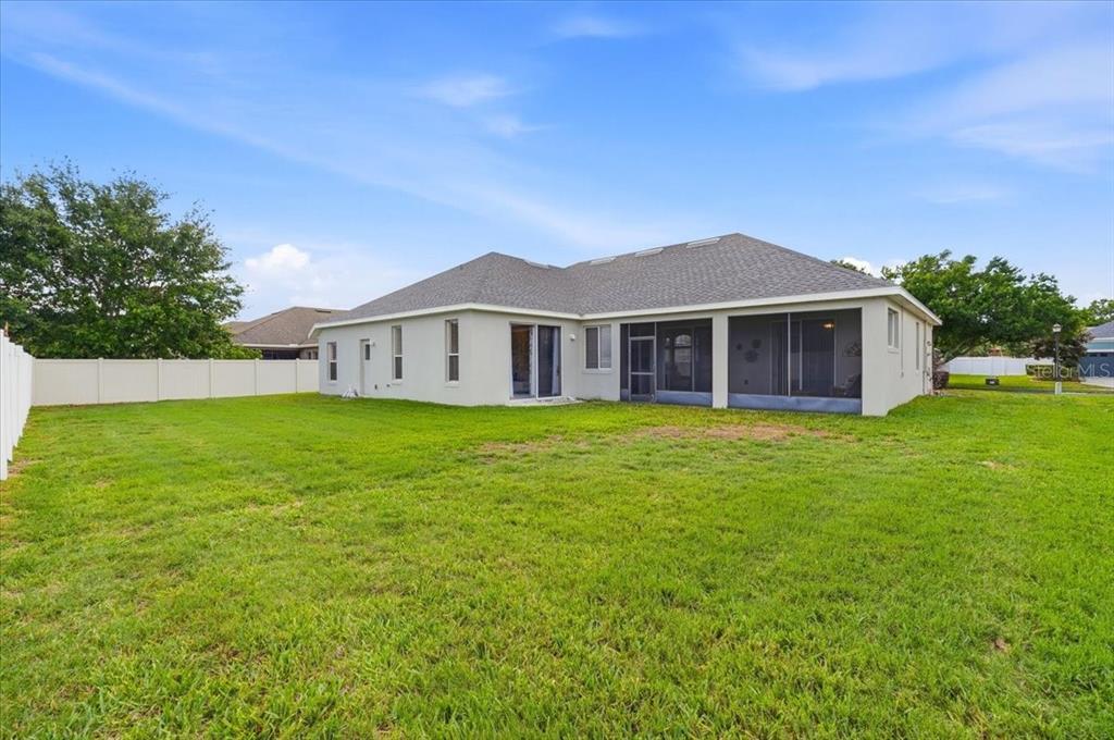 The exterior of a single-story house features a screened-in lanai and a large backyard — 445 AMETHYST AVENUE, AUBURNDALE, FL