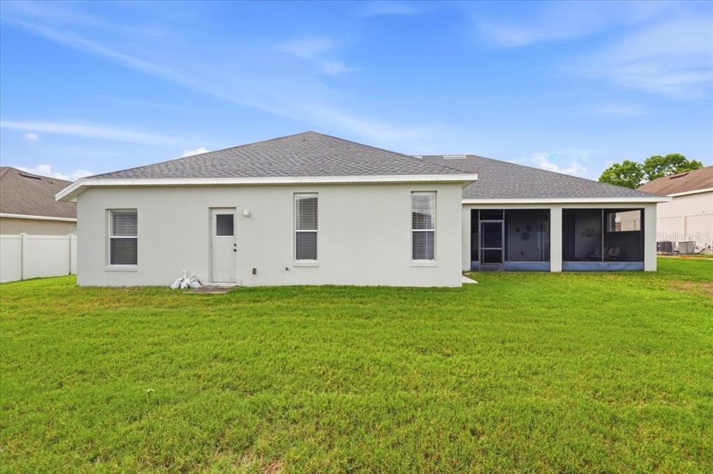 The back exterior of a single-story house features a screened-in porch and a grassy yard — 445 AMETHYST AVENUE, AUBURNDALE, FL