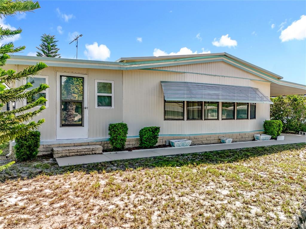 Exterior view of a single-story manufactured home with light siding and a metal awning — 1440 NASSAU CIRCLE, TAVARES, FL