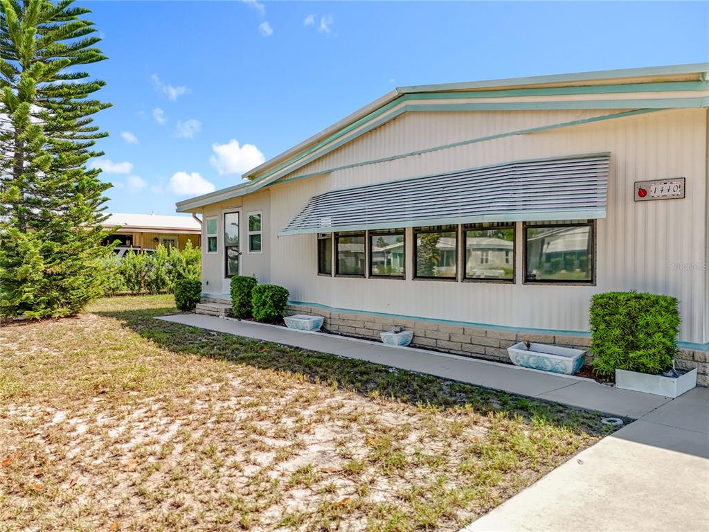 A single-story mobile home with light siding, a metal window awning, and a concrete walkway — 1440 NASSAU CIRCLE, TAVARES, FL