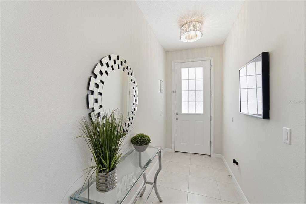 A bright entryway features a glass console table, a round decorative mirror, and tile flooring — 9013 EGRET MILLS TERRACE, KISSIMMEE, FL