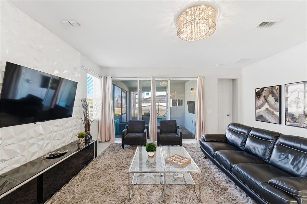 A living room features a black leather sofa, glass coffee table, and textured accent wall — 9013 EGRET MILLS TERRACE, KISSIMMEE, FL