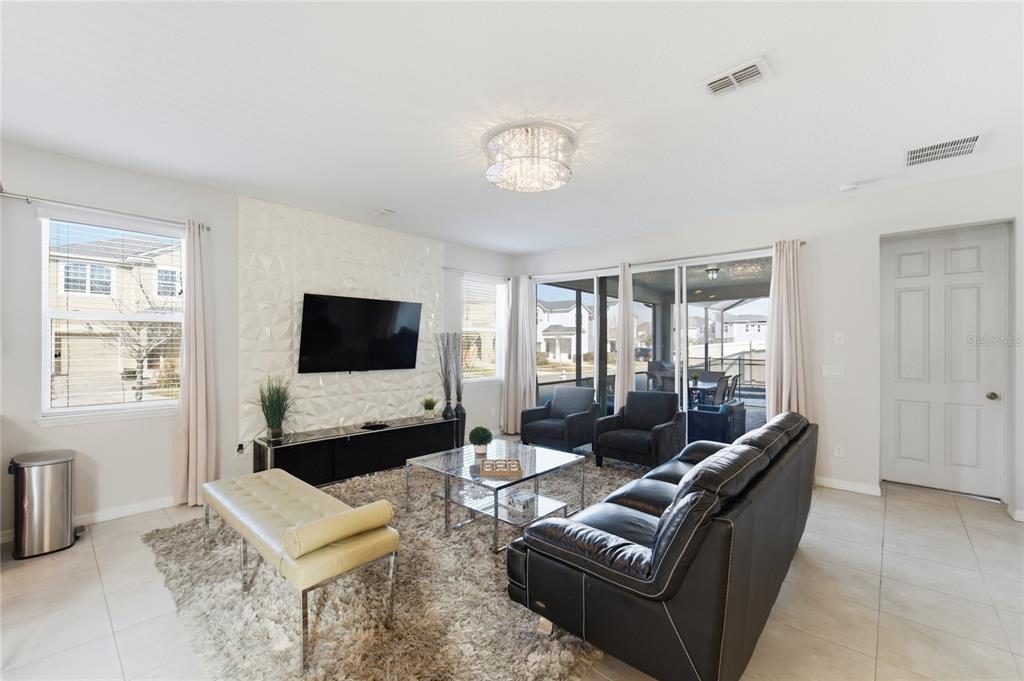 A living room features a textured accent wall, a television, and a glass coffee table — 9013 EGRET MILLS TERRACE, KISSIMMEE, FL