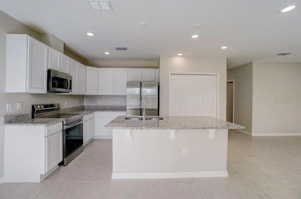 A kitchen features white cabinets, granite countertops, stainless steel appliances, and a central island — 31571 WILD GRAPE LANE, BROOKSVILLE, FL