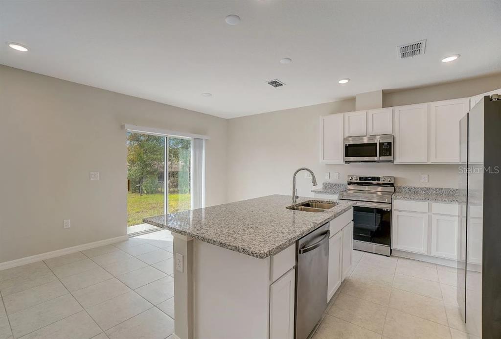 A kitchen with white cabinets, granite countertops, a center island, and a sliding glass door — 31571 WILD GRAPE LANE, BROOKSVILLE, FL