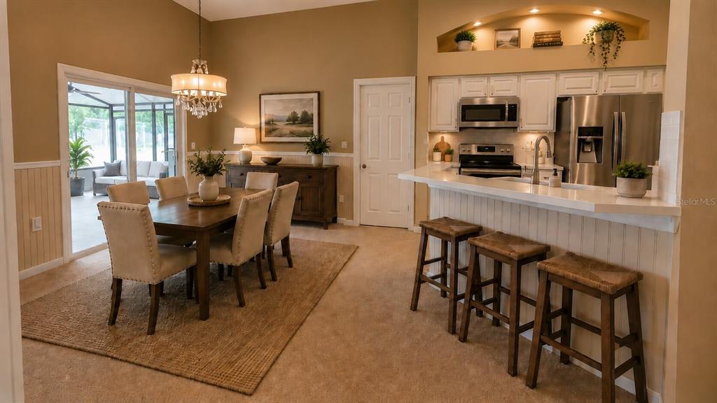 A dining area with a wooden table and chairs sits adjacent to a kitchen with stools — 649 BUCKINGHAM DRIVE, OVIEDO, FL