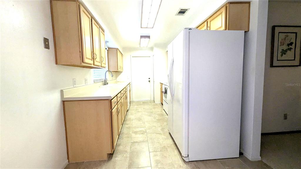 A galley kitchen features light wood cabinets, white countertops, and a white refrigerator — 8067 SWEETGUM LOOP, ORLANDO, FL