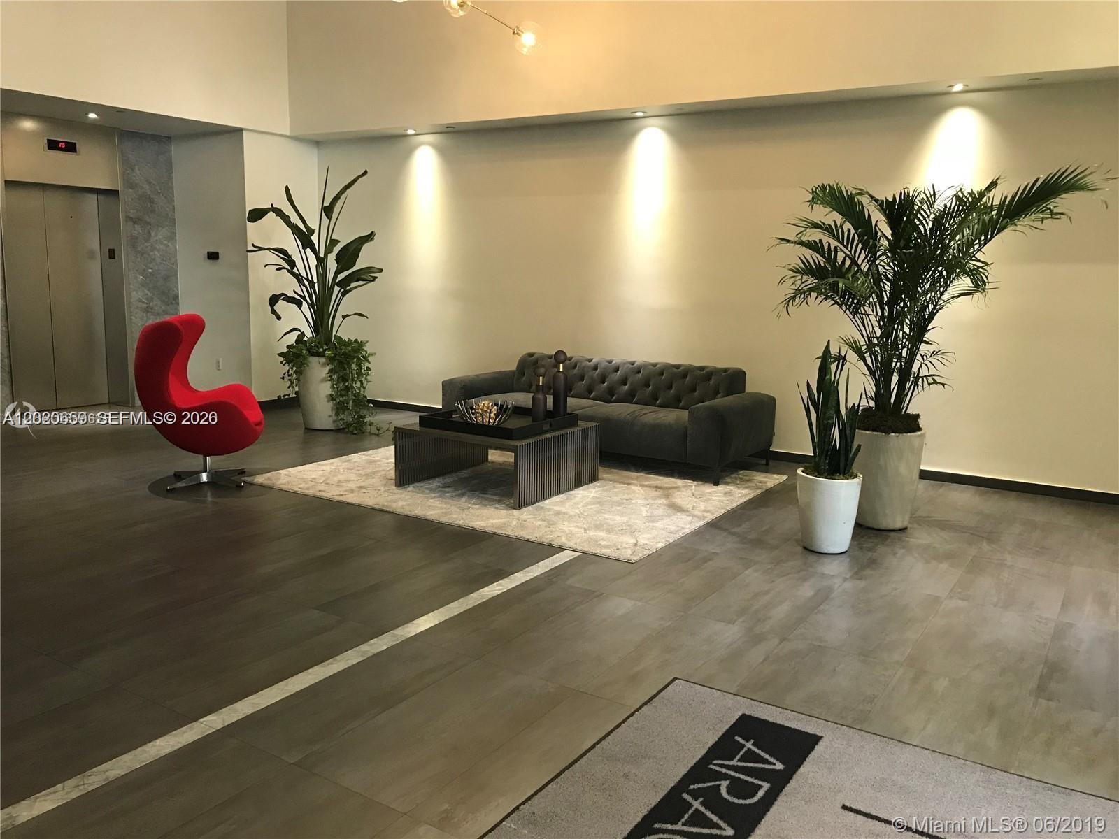 A modern lobby features a gray tufted sofa, a red egg chair, and potted plants — 10 Aragon Ave # 1018, Coral Gables FL 33134, CORAL GABLES, FL