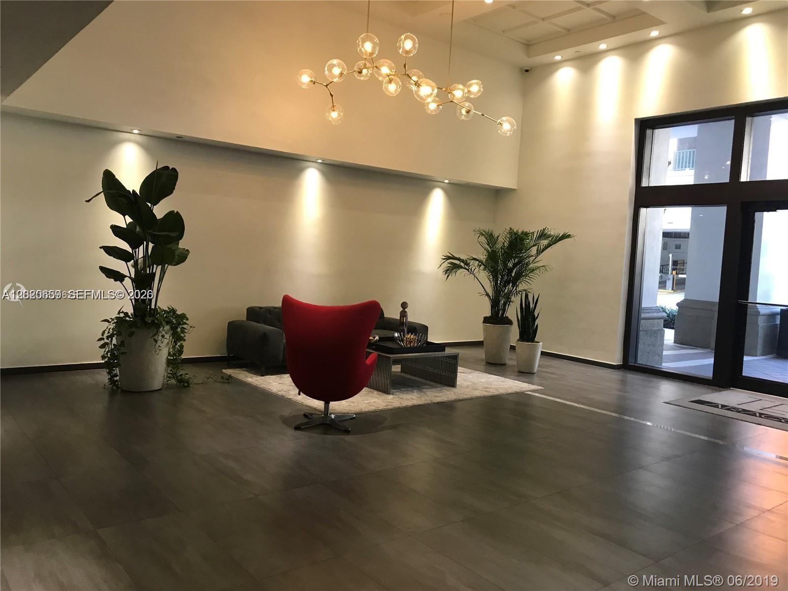 A modern lobby features a red egg chair, a gray sofa, and a branching chandelier — 10 Aragon Ave # 1018, Coral Gables FL 33134, CORAL GABLES, FL
