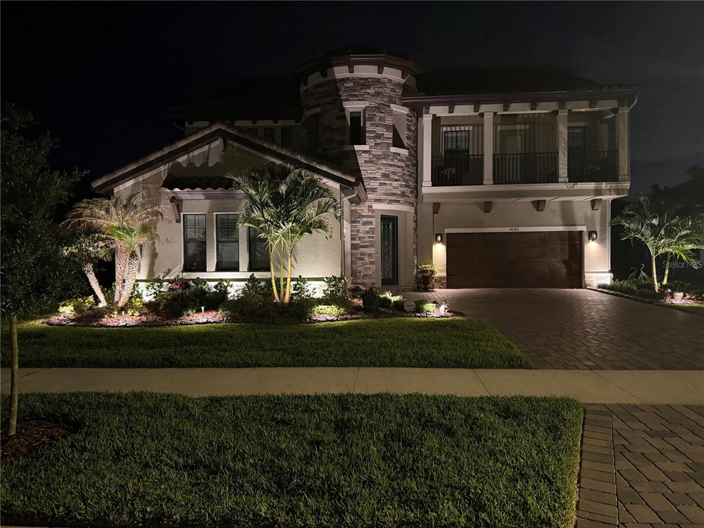 A two-story house with a stone turret, balcony, and illuminated landscaping at night — 4285 STAR VIEW PLACE, BRANDON, FL
