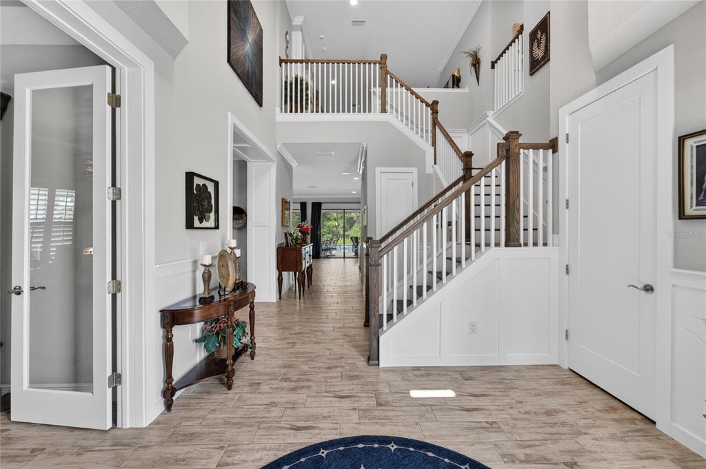 A bright foyer features wood-look tile flooring, a white staircase, and a view toward the back — 4285 STAR VIEW PLACE, BRANDON, FL
