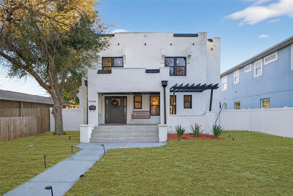 A two-story white stucco house features a front porch, a pergola, and a grassy yard — 6566 1ST AVENUE S, ST PETERSBURG, FL