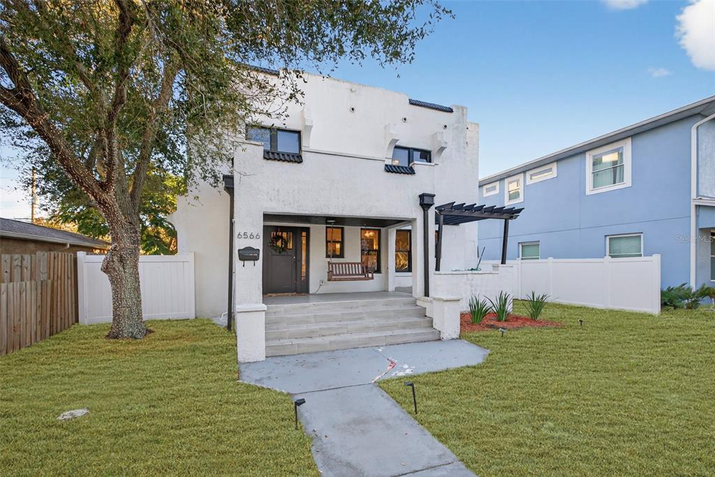 A two-story white stucco house features a covered front porch with a hanging swing — 6566 1ST AVENUE S, ST PETERSBURG, FL