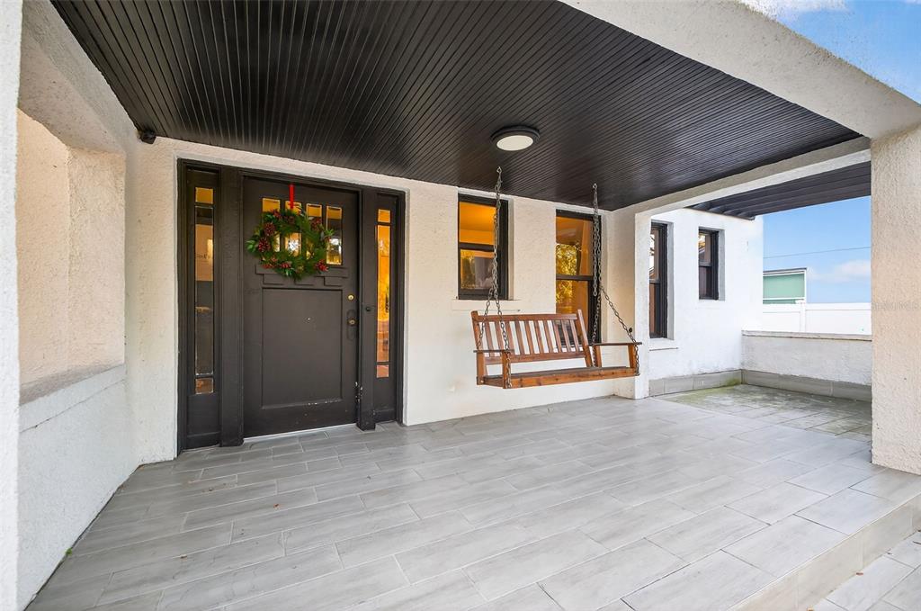 A covered front porch features a wooden swing, a dark front door, and tiled flooring — 6566 1ST AVENUE S, ST PETERSBURG, FL