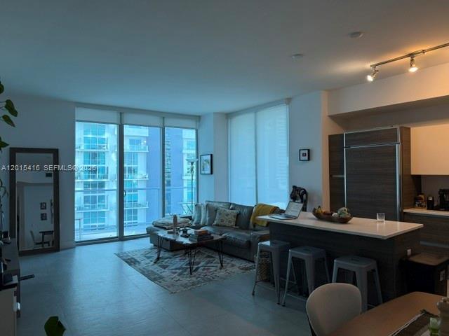 A modern living room features a gray sofa, kitchen island with stools, and floor-to-ceiling windows — 1100 S Miami Ave # 801, Miami FL 33130, MIAMI, FL