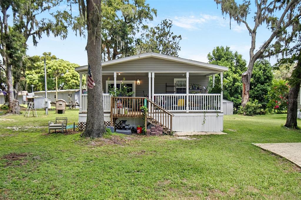 A single-story house with a covered front porch and white railings sits on a grassy lot — 123 MAGNOLIA DRIVE, SATSUMA, FL