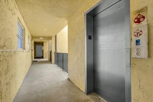 An outdoor apartment hallway features a metal elevator door and a beige stucco wall — 15430 SW 82nd Ln # 625, Miami FL 33193, MIAMI, FL