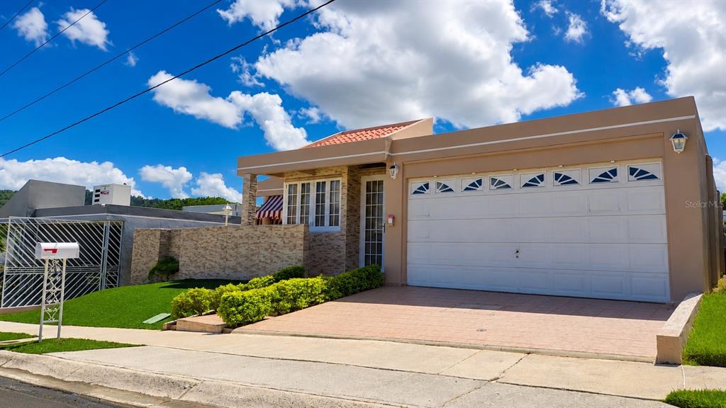 A tan single-story house with a two-car garage, stone facade, and a manicured hedge — Calle G #P15 GOLDEN GATE II, CAGUAS, PR