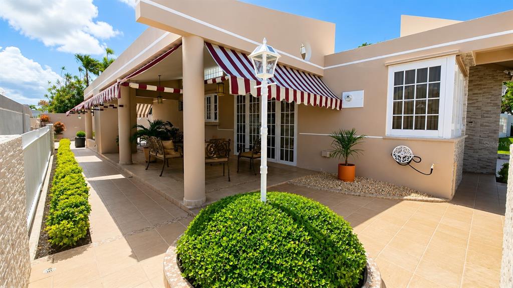 A patio with a striped awning, outdoor furniture, and a central manicured shrub — Calle G #P15 GOLDEN GATE II, CAGUAS, PR