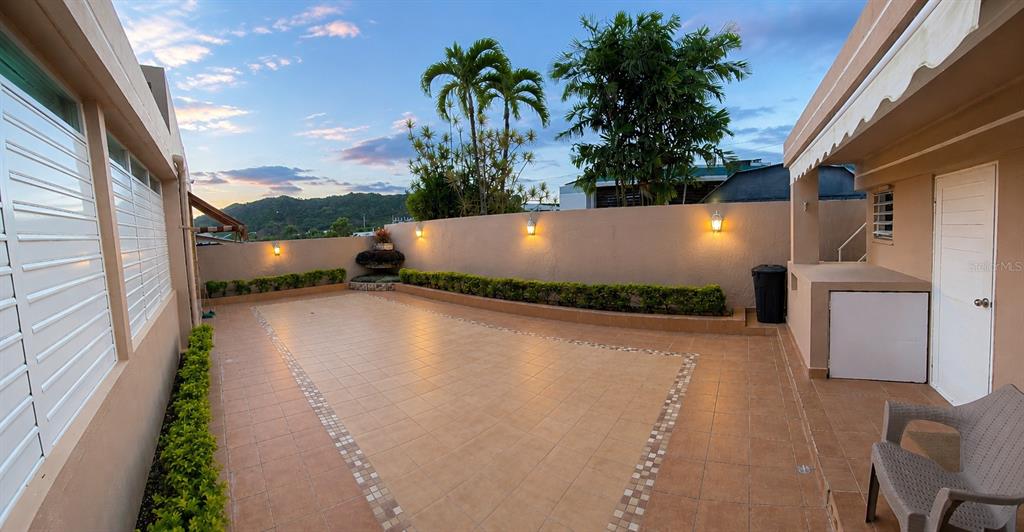 A paved outdoor patio features a low wall, landscaping, and exterior lighting at dusk — Calle G #P15 GOLDEN GATE II, CAGUAS, PR