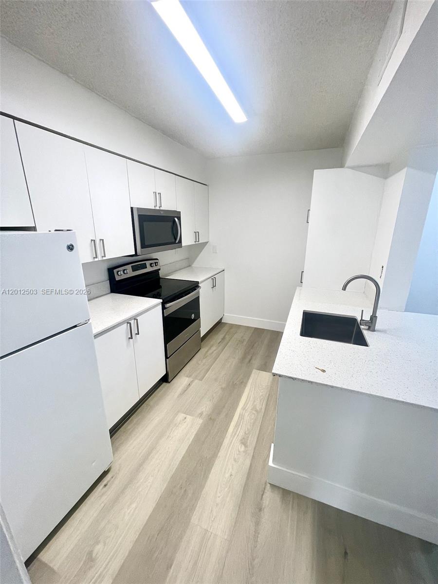 A modern kitchen features white cabinets, stainless steel appliances, and light wood-look flooring — 15201 SW 80th St # 205, Miami FL 33193, MIAMI, FL
