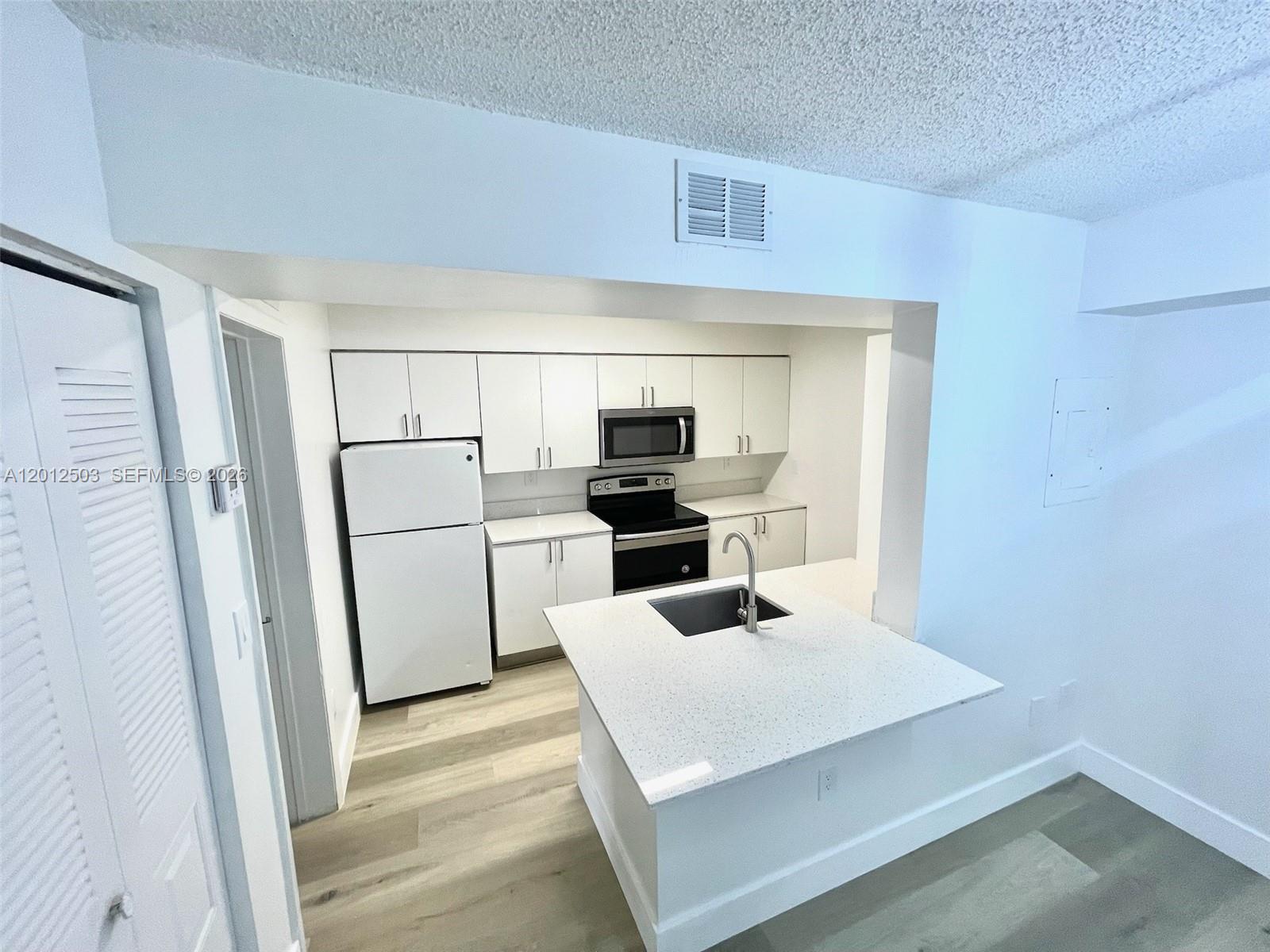 A kitchen features white cabinets, stainless steel appliances, and a central island with a sink — 15201 SW 80th St # 205, Miami FL 33193, MIAMI, FL