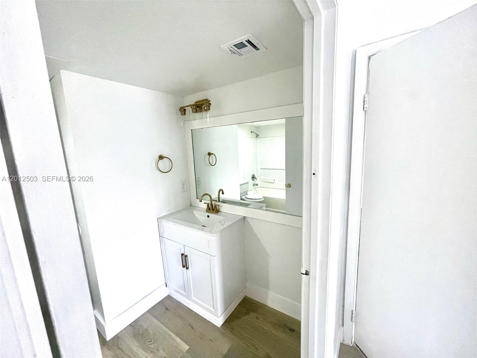 A bathroom features a white vanity, gold faucet, wall-mounted mirror, and light wood-look flooring — 15201 SW 80th St # 205, Miami FL 33193, MIAMI, FL