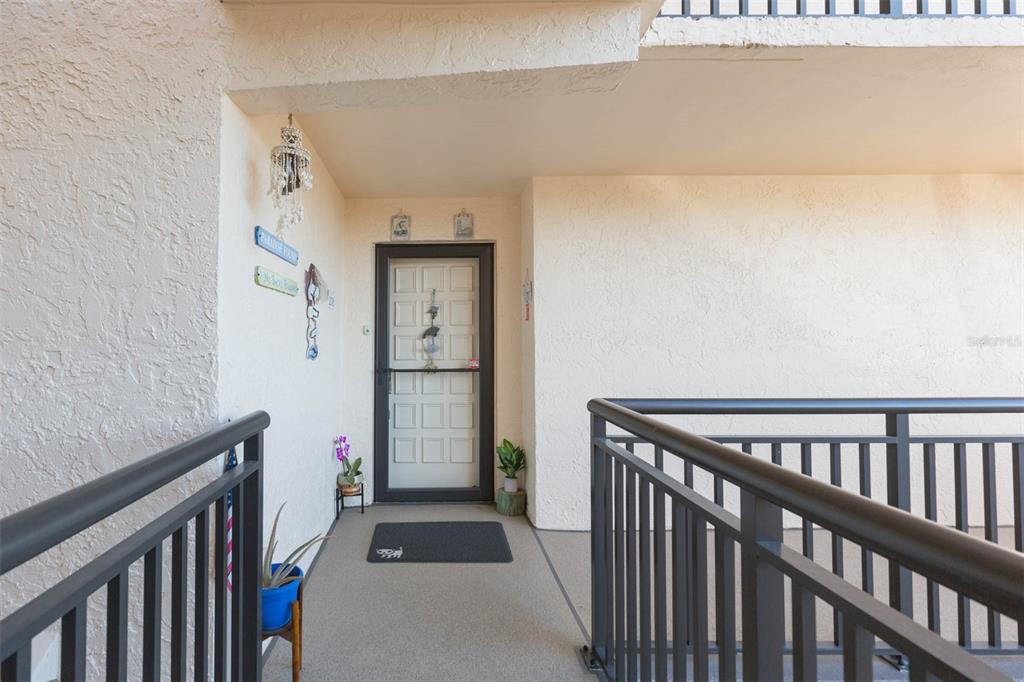 An exterior view of a residential entryway with a white door and dark metal railings — 5633 PUERTA DEL SOL BOULEVARD S UNIT 208, ST PETERSBURG, FL