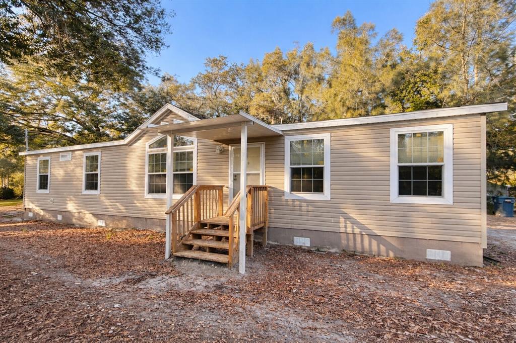 A tan vinyl-sided manufactured home with a wooden front porch and stairs — 16744 RACE TRACK ROAD, ODESSA, FL