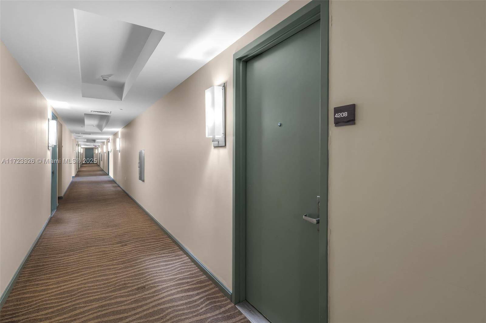 A long, carpeted apartment hallway features beige walls, recessed ceiling lighting, and a green door — 50 Biscayne Blvd # 4208, Miami FL 33132, MIAMI, FL