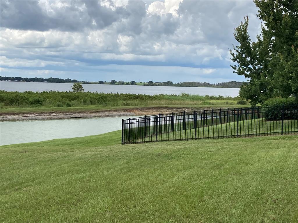 A black metal fence separates a grassy lawn from a canal and a large lake — 493 ADAMS VIEW LANE, AUBURNDALE, FL