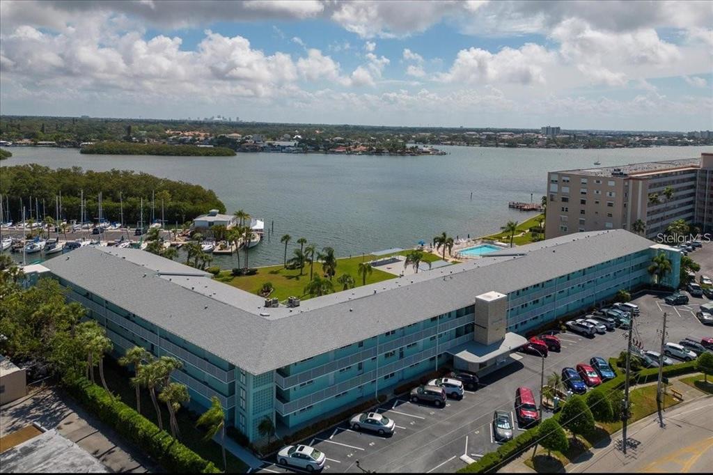 An aerial view shows a multi-story apartment building with a parking lot and waterfront pool — 1819 SHORE DRIVE S UNIT 110, SOUTH PASADENA, FL
