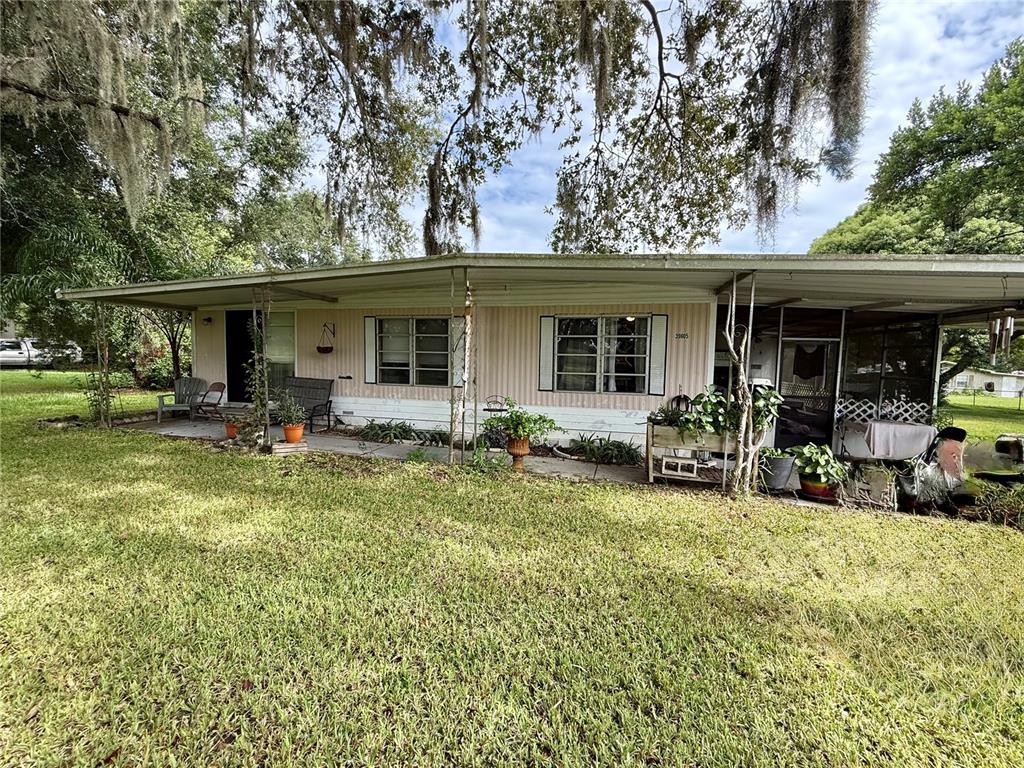 A single-story mobile home with a covered porch and carport sits on a grassy lot — 39605 OTIS ALLEN ROAD, ZEPHYRHILLS, FL