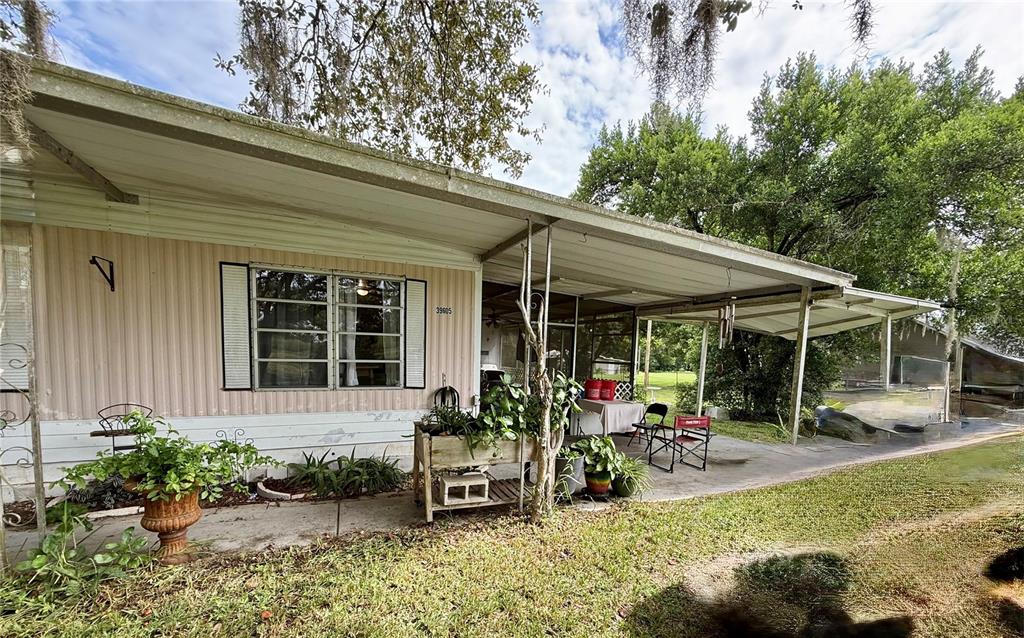 A single-story mobile home features a covered patio, a wooden planter, and a grassy yard — 39605 OTIS ALLEN ROAD, ZEPHYRHILLS, FL