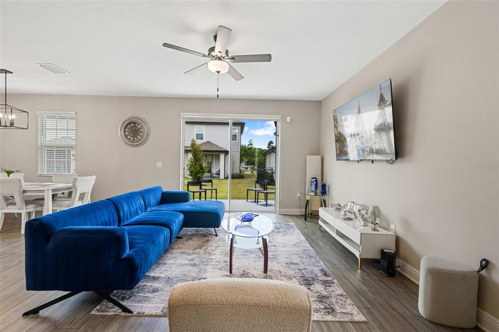A living room features a blue sectional sofa, a glass coffee table, and a wall-mounted television — 7745 SOMERSWORTH DRIVE, KISSIMMEE, FL