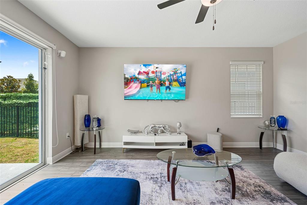 A living room features a wall-mounted television, a white media console, and a glass coffee table — 7745 SOMERSWORTH DRIVE, KISSIMMEE, FL