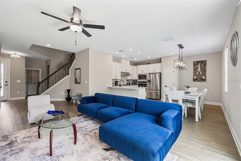 An open-concept living room and kitchen feature a blue sectional sofa and wood-look flooring — 7745 SOMERSWORTH DRIVE, KISSIMMEE, FL