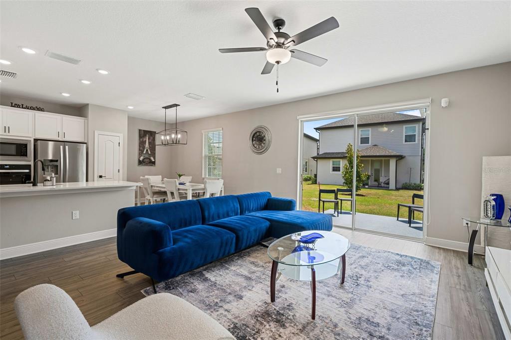 A living room with a blue sectional sofa, glass coffee table, and sliding doors to a yard — 7745 SOMERSWORTH DRIVE, KISSIMMEE, FL