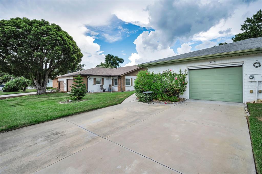 A concrete driveway leads to a house with a green garage door and landscaping — 3215 MCMATH DRIVE, PALM HARBOR, FL