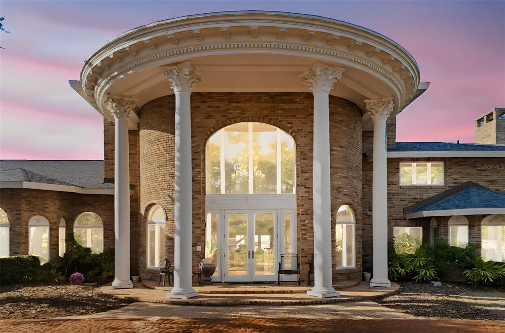 A brick house features a circular entrance with tall white columns and a large arched window — 6118 RIVERVIEW BOULEVARD, BRADENTON, FL