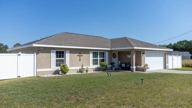 A single-story house with a tan stucco exterior, a two-car garage, and a white fence — 227 OAK LANE LOOP, OCALA, FL