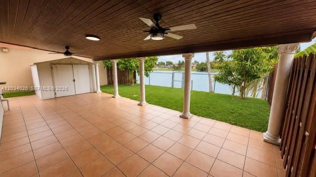 A covered patio with tiled flooring, ceiling fans, and columns overlooks a grassy backyard lakefront — 12211 SW 137th Ter, Miami FL 33186, MIAMI, FL