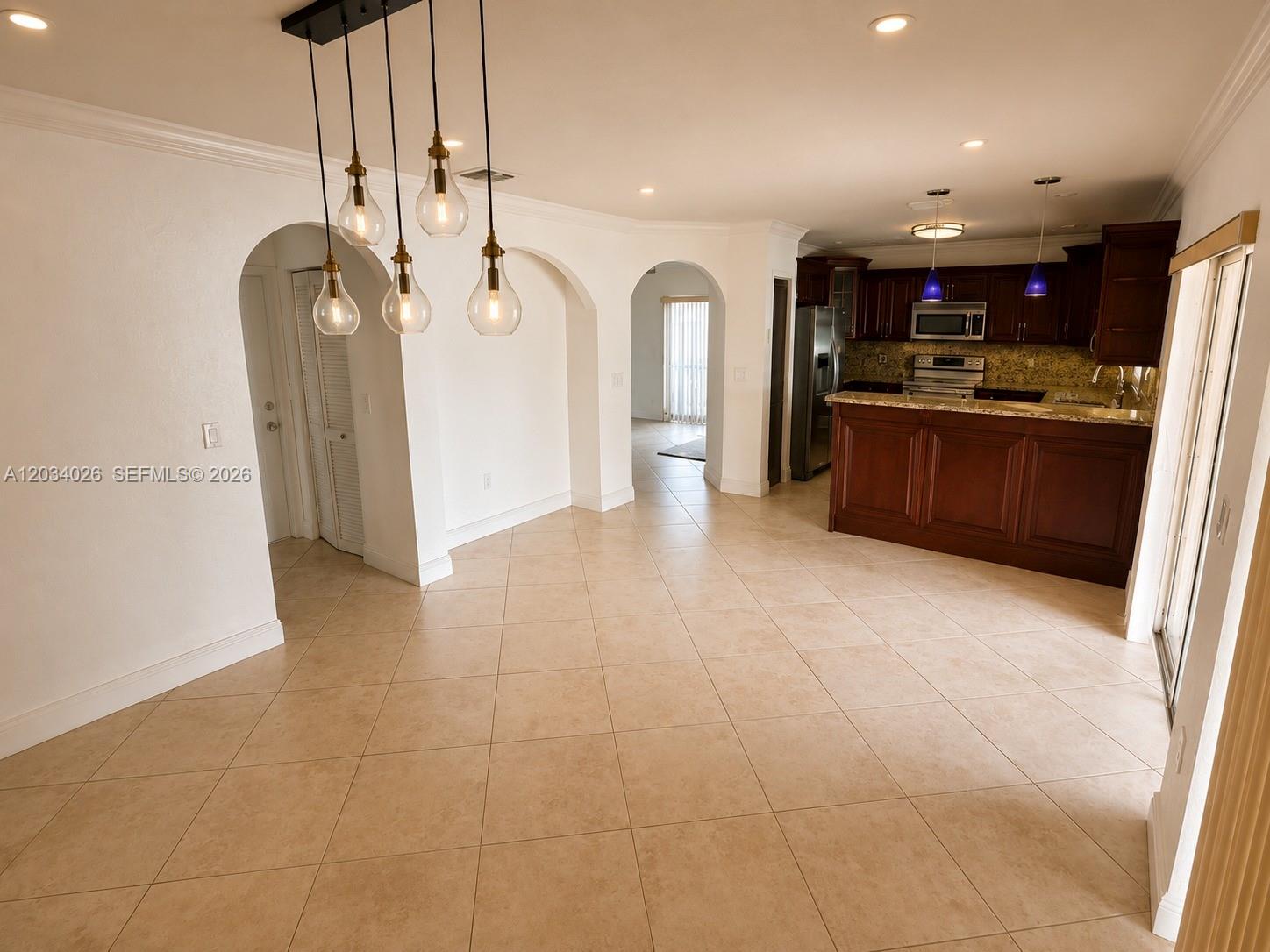 An open-concept dining area features tile flooring, arched doorways, and a dark wood kitchen — 12211 SW 137th Ter, Miami FL 33186, MIAMI, FL