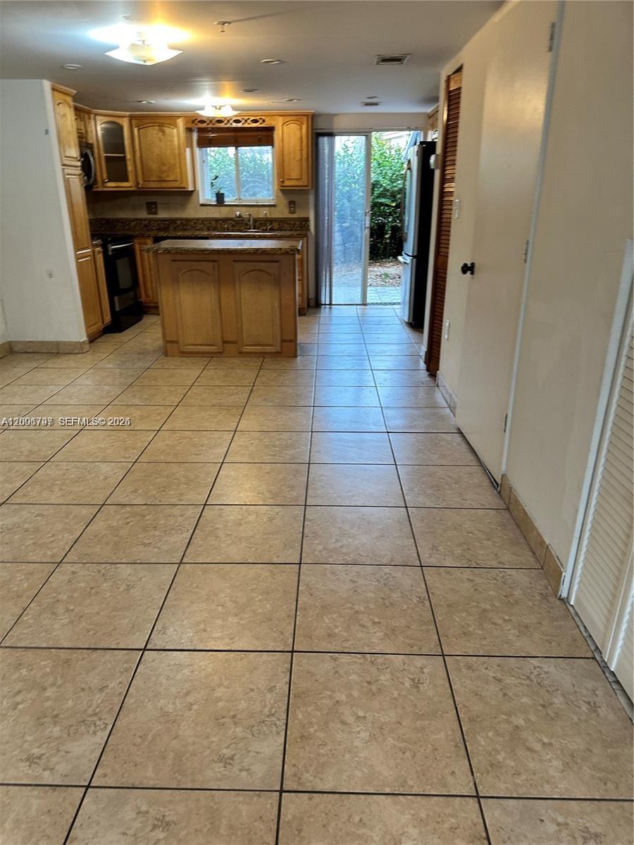 A kitchen features light wood cabinets, a small island, and tile flooring leading to a patio — 551 NW 82nd Ave # 502, Miami FL 33126, MIAMI, FL