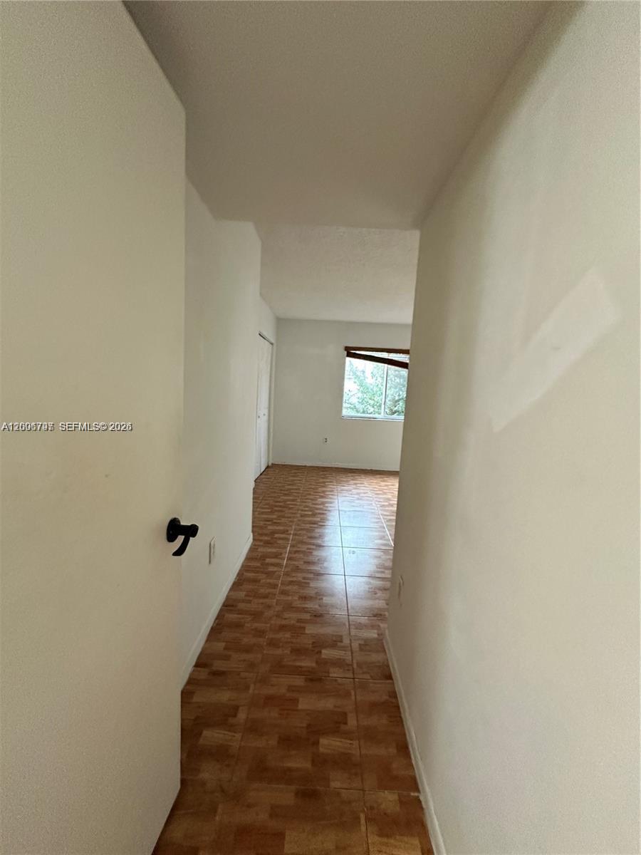 A narrow hallway with light-colored walls leads to a bedroom with wood-look tile flooring — 551 NW 82nd Ave # 502, Miami FL 33126, MIAMI, FL