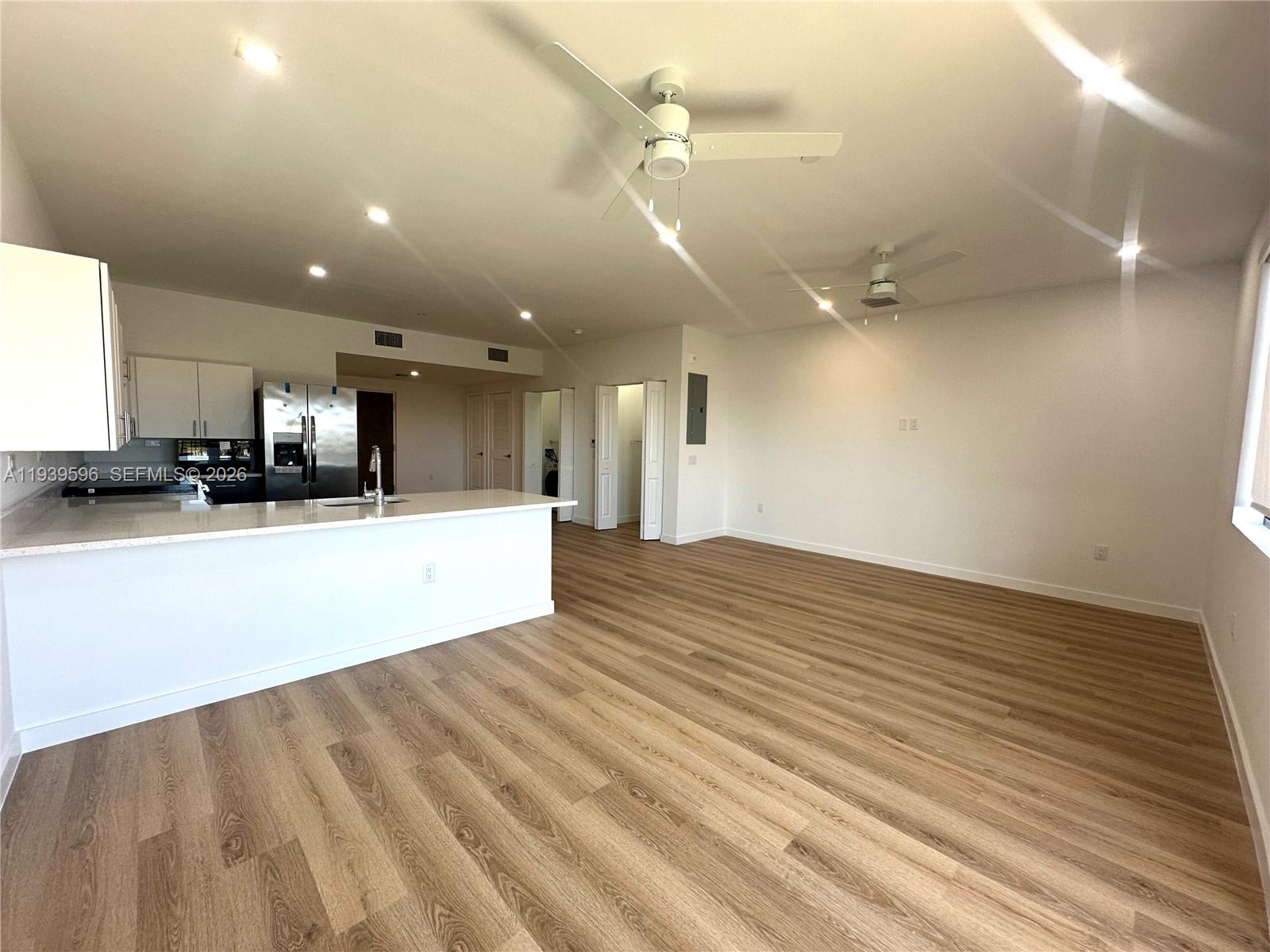 An open-concept kitchen and living area features white cabinetry, stainless steel appliances, and wood-look flooring — 20 NE 19th Ave, Pompano Beach FL 33060, POMPANO BEACH, FL